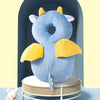 A soft blue baby head protector pillow with yellow wings is displayed on a white stand.