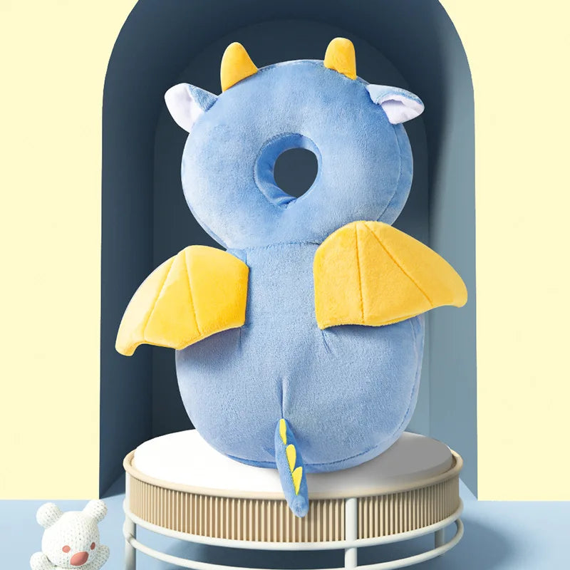 A soft blue baby head protector pillow with yellow wings is displayed on a white stand.