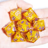A hand holds a set of yellow resin polyhedral dice showing various numbers and symbols.