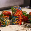 A close-up of seven frosted crack resin polyhedral dice in various colors including green, red, and blue.