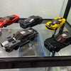 A collection of various die-cast or model cars in red, black, and yellow colors displayed in a glass case.