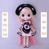 A pink-haired fashion doll with black hair accessories and a pink dress, displayed against a light gray background.