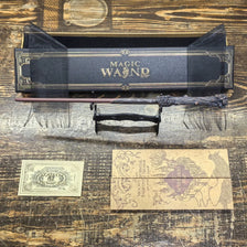 An anime-inspired magic wand with a dark handle and metal core is displayed in a black presentation box on a wooden surface.
