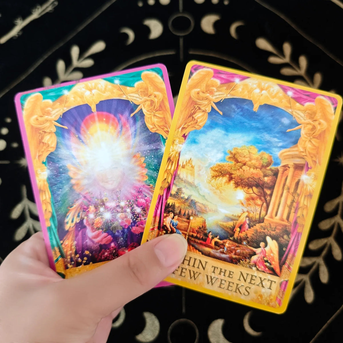 A hand holds a yellow oracle deck featuring an illustration of a bright, glowing sun and landscape.