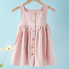 A pink linen jumper dress for a toddler girl hanging on a wooden hanger against a light blue background.