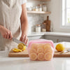 A hand cuts a silicone storage bag filled with sliced lemons on a wooden board in a kitchen setting.