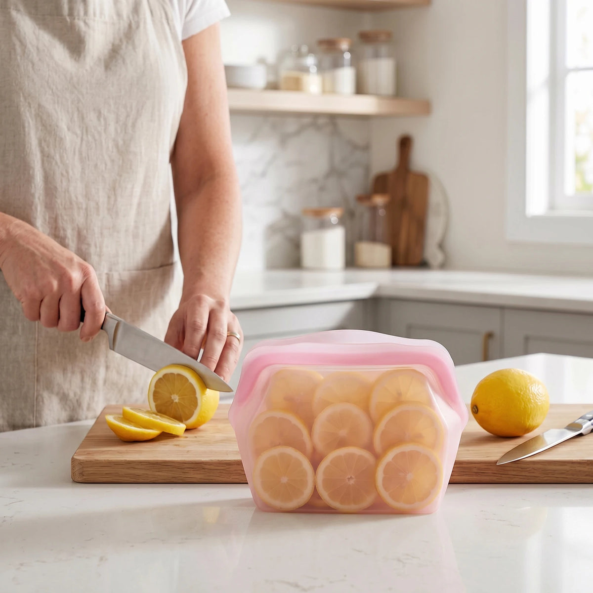 A hand cuts a silicone storage bag filled with sliced lemons on a wooden board in a kitchen setting.