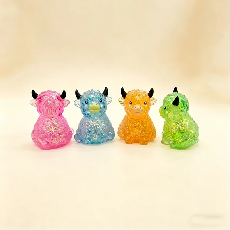 Four glitter squishy toys shaped like Highland cows in pink, blue, orange, and green.