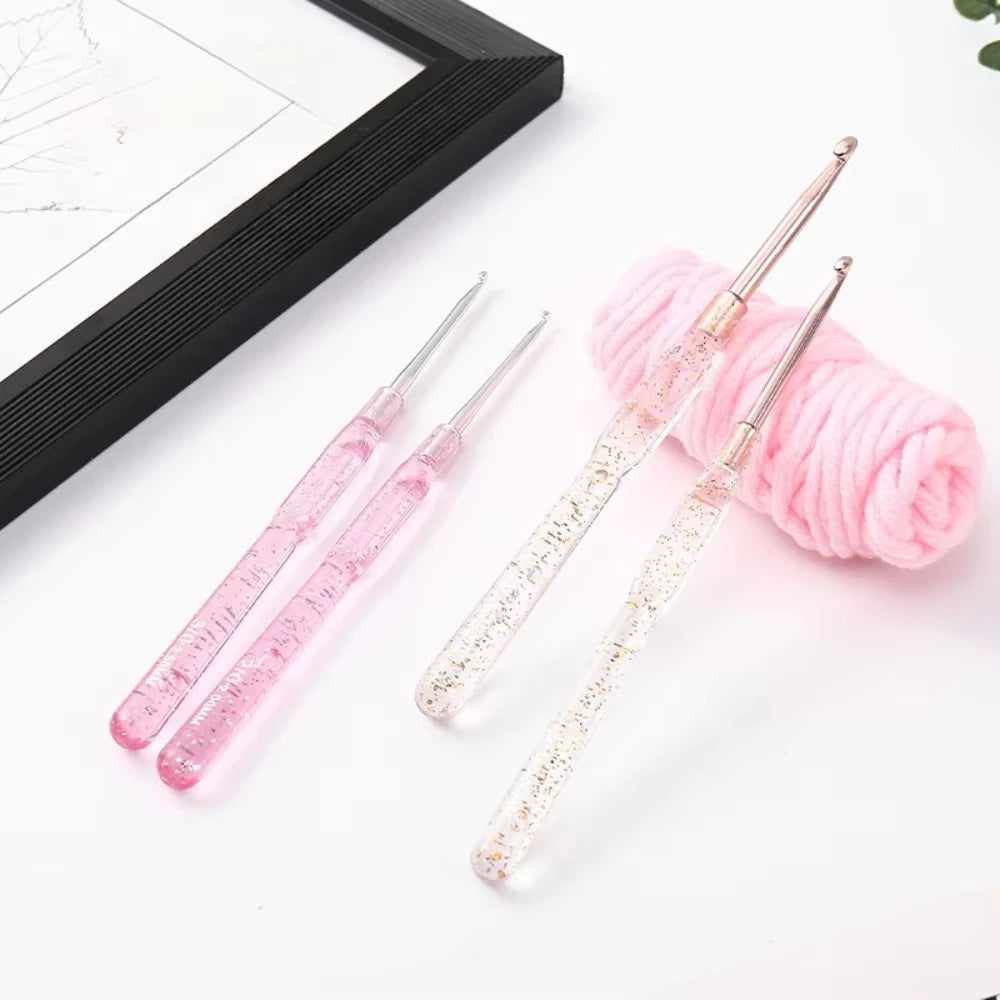 A set of seven clear and pink aluminum crochet hooks with color-coded handles resting on a white surface next to a pink yarn 