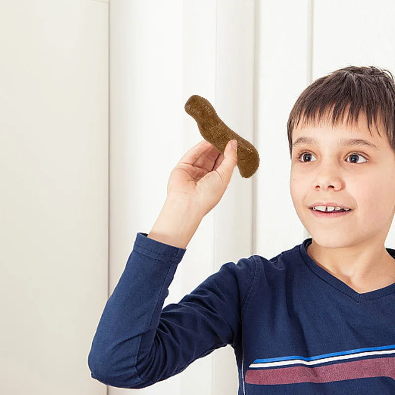 Un jeune garçon tient un jouet de défécation brun et réaliste vers la caméra.