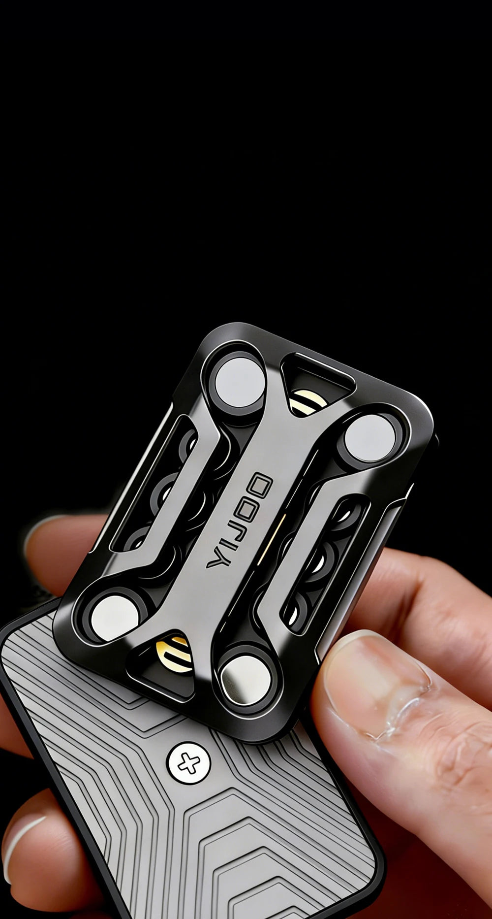 A hand holds a black metal magnetic fidget slider device against a gray textured background.