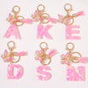 A set of initial heart keychains featuring pink glitter acrylic letters and gold hardware with pink feather butterfly charms.