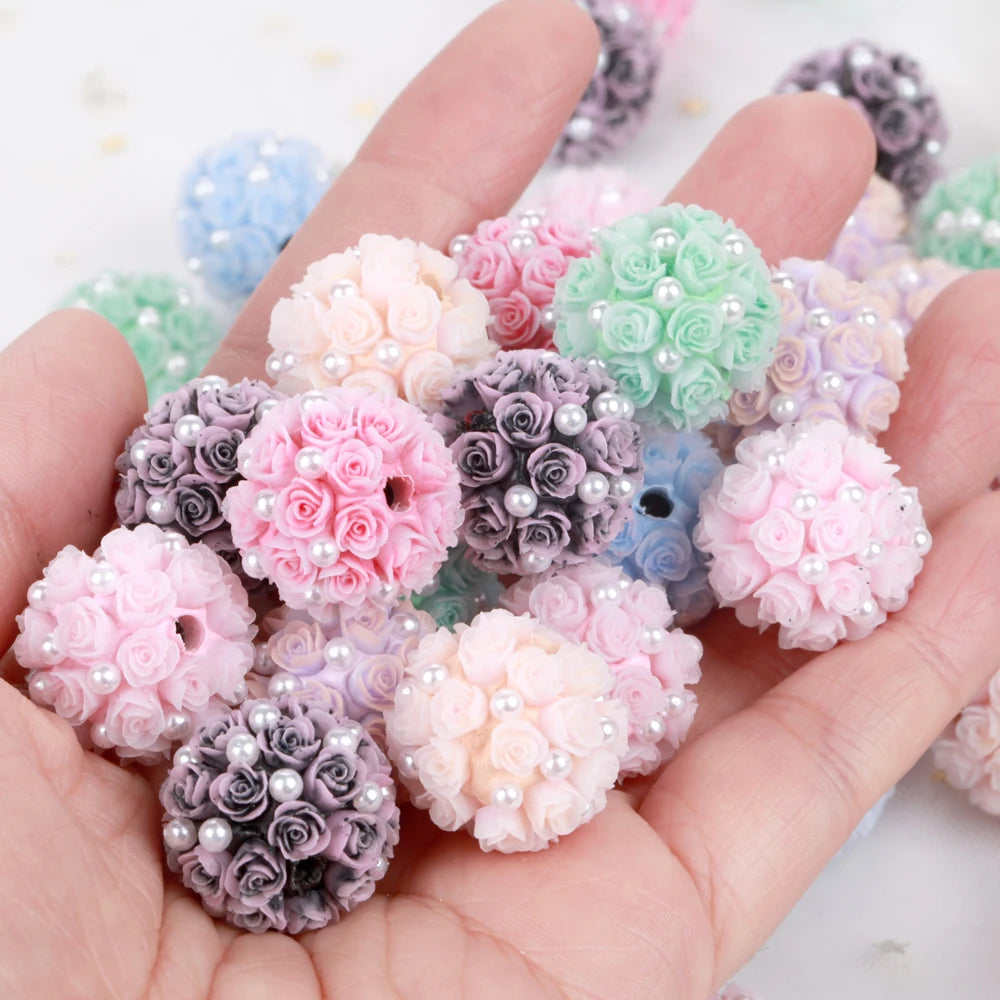 A hand holds a variety of pink, purple, and green rose flower ball acrylic beads for jewelry making.