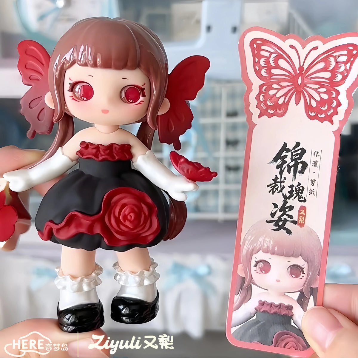 A collectible figurine of a girl with pink hair and red butterfly wings, dressed in black and white, displayed next to a prod