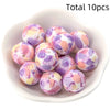 A bowl filled with ten pieces of round, printed silicone beads in shades of purple, pink, and yellow for DIY jewelry making.