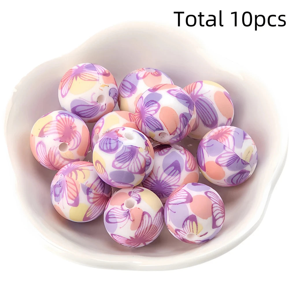 A bowl filled with ten pieces of round, printed silicone beads in shades of purple, pink, and yellow for DIY jewelry making.