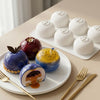 A white silicone mold is shown alongside various colorful fruits and golden utensils on a light surface.