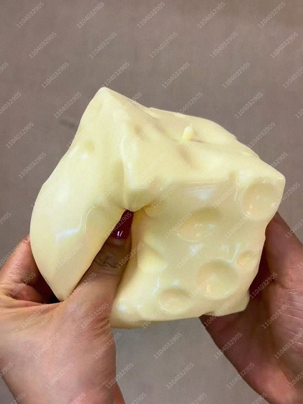 A hand is squeezing a large, pale yellow cheese cube stress ball.