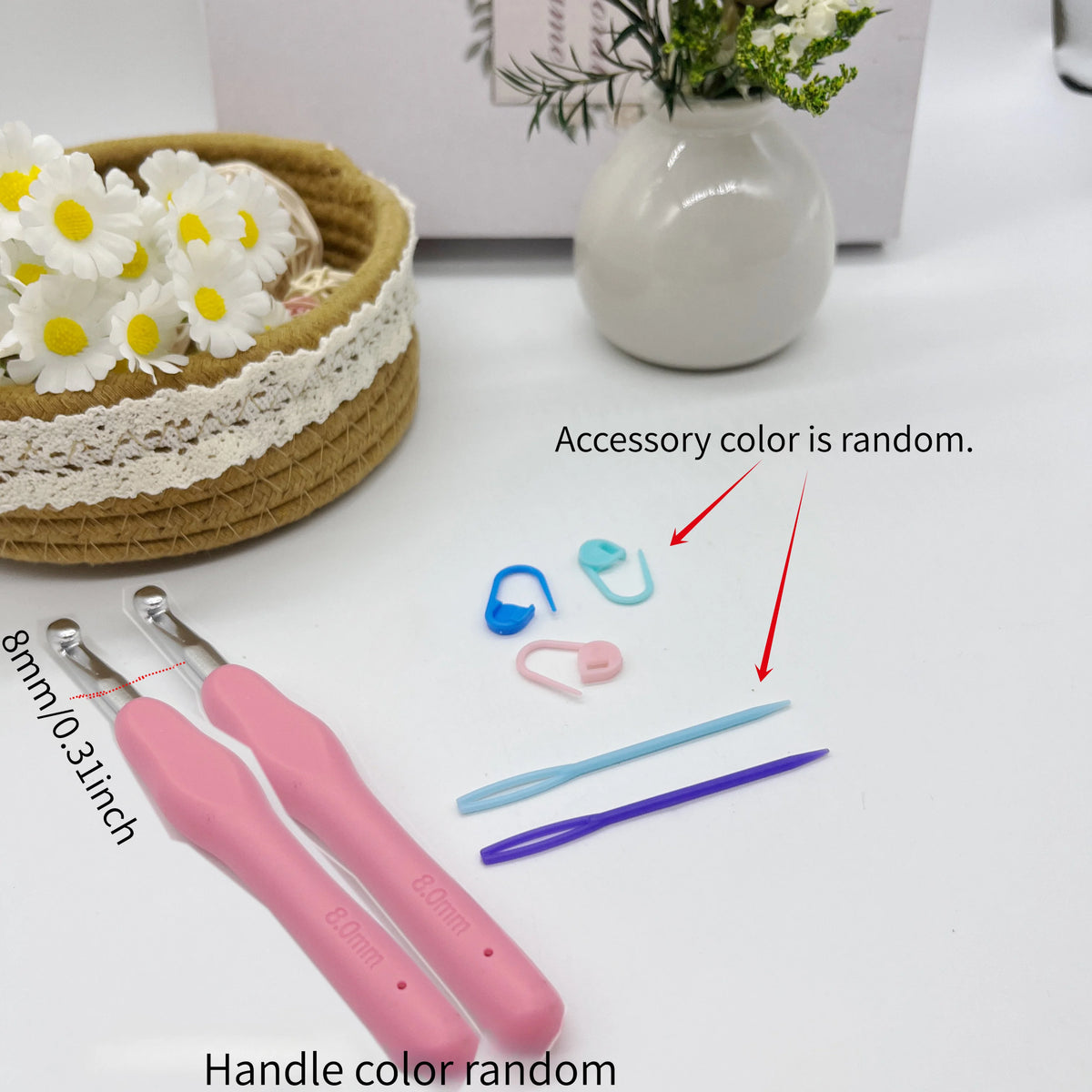 A set of pink crochet hooks with stitch markers and needles, along with a white vase and some white flowers.