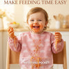 A smiling baby wearing a pink bib with a mess-free pocket, demonstrating easy feeding.