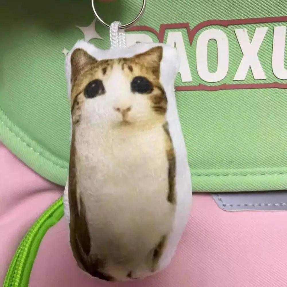 A white and brown cat plush keychain with large eyes is attached to a silver keyring.