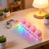 A clear acrylic keychain featuring pink silicone fidget cubes that glow with a rainbow of light.