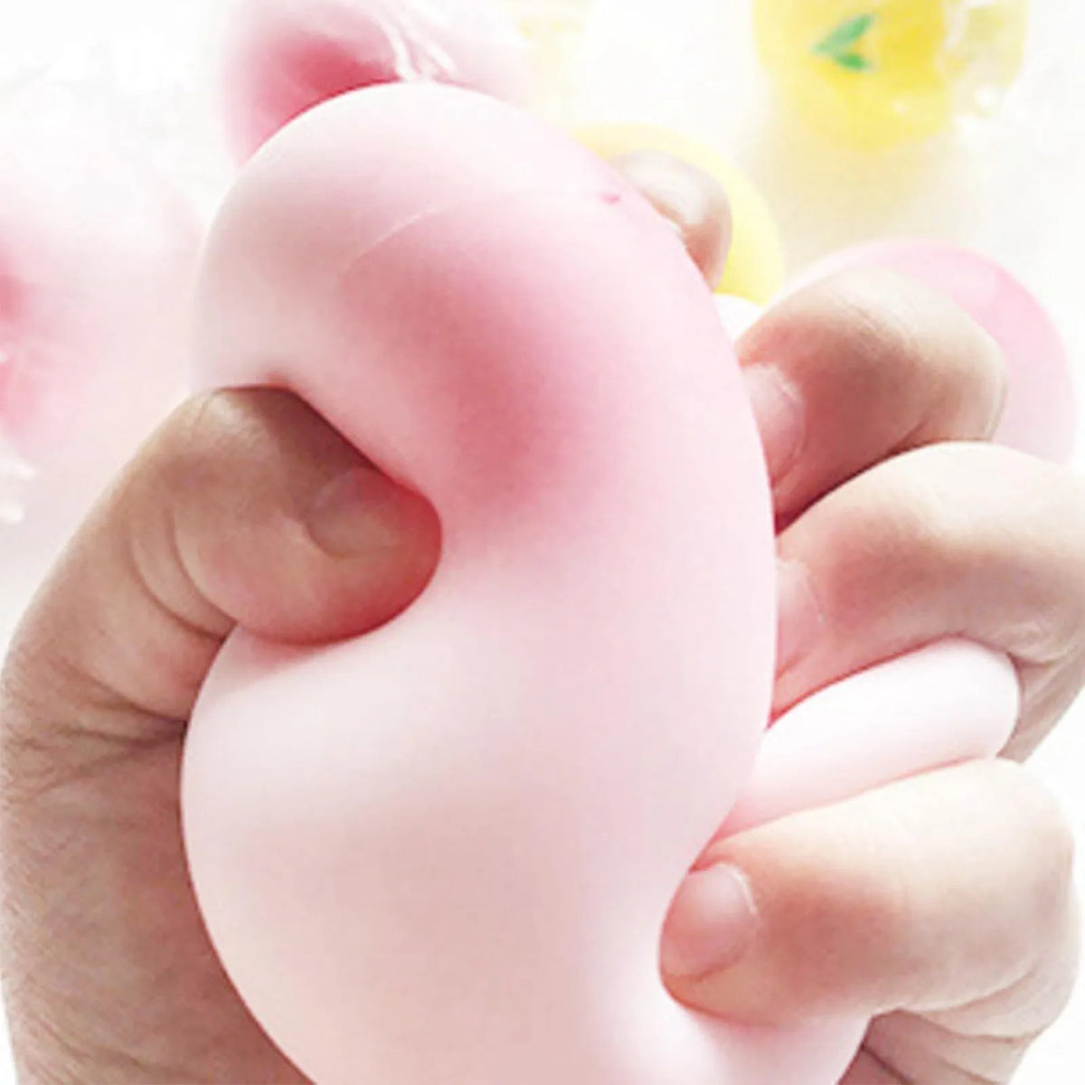 A hand is squeezing a pink peach-shaped squishy stress relief toy.