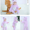 A baby wearing a purple animal hooded romper sitting on a wooden toy horse.