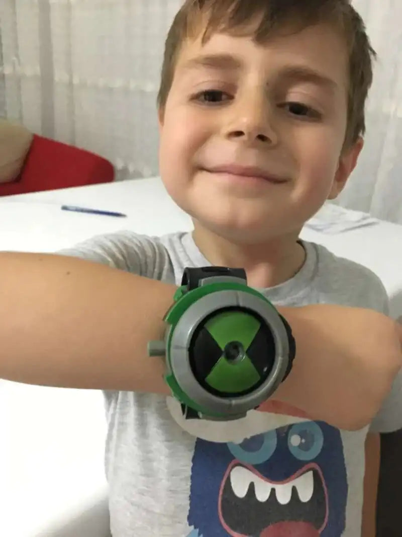 A young boy is holding a green and black watch toy, the Ben 10 Omnitrix Projector Watch Toy, in front of him.