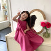 A young girl wearing a pink sleeveless cotton sundress poses in front of a large mirror.