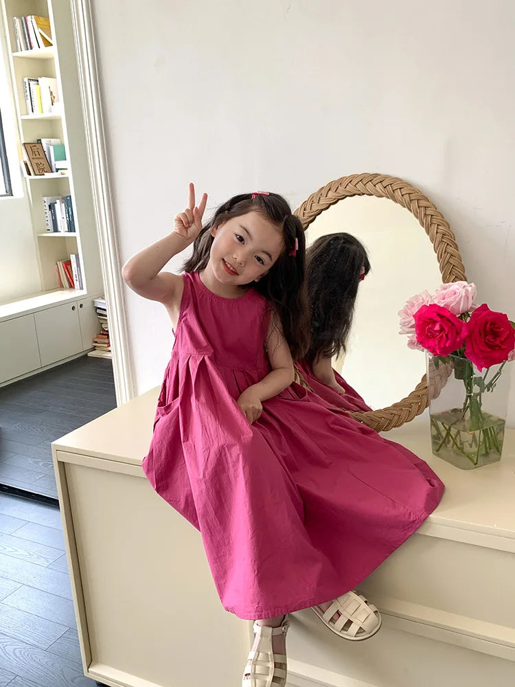 A young girl wearing a pink sleeveless cotton sundress poses in front of a large mirror.