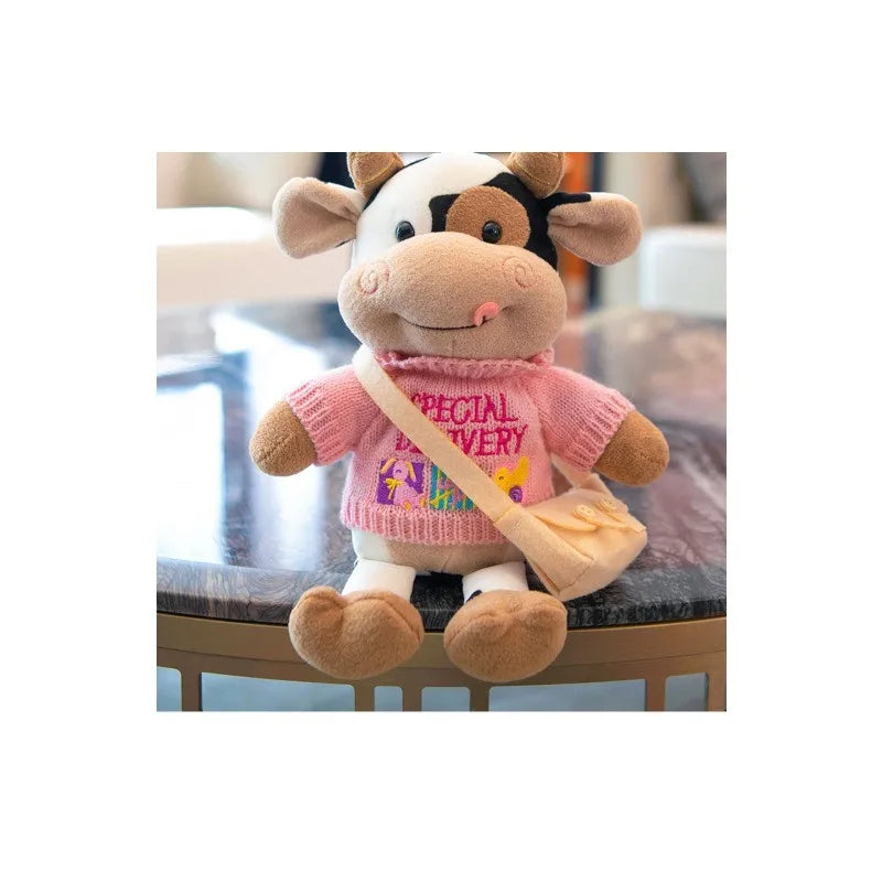 A soft cow plush toy with white and brown markings wearing a pink shirt and carrying a tan bag.