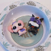 A set of three small figures, including a pink bunny and a black cat with purple glasses, displayed in a light blue bowl.