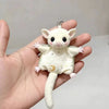 A small white plush mouse charm with a gold keyring and a crescent moon design is held in a hand.