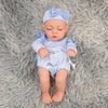 A lifelike soft vinyl reborn doll with a light blue bow and matching outfit lying on a gray fluffy surface.