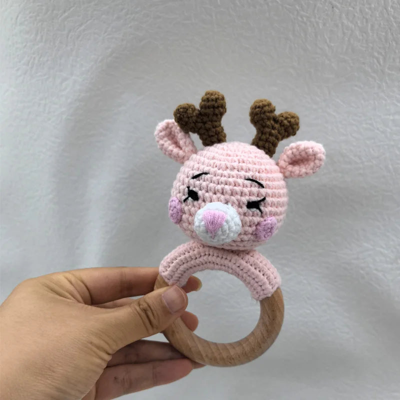 A handmade pink otter rattle and teether ring with brown antlers is held in a hand.