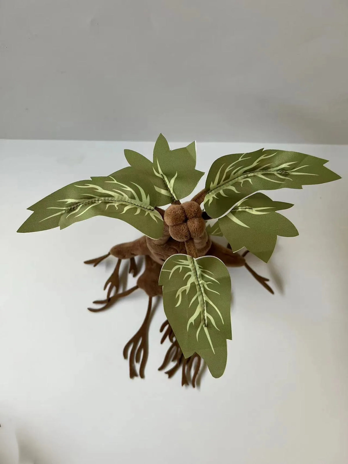 A plush toy resembling a mandrake plant with large green leaves and brown roots.