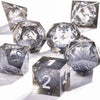 A set of handmade polyhedral dice with a galaxy finish scattered on a white surface.