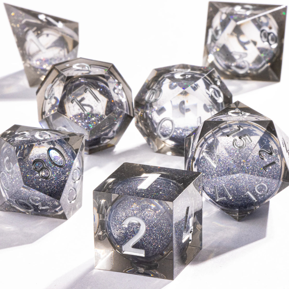 A set of handmade polyhedral dice with a galaxy finish scattered on a white surface.