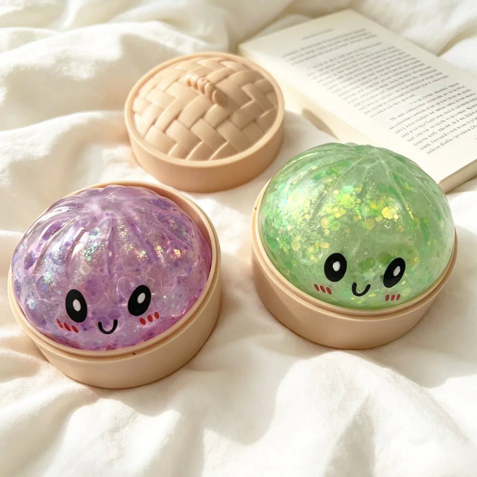 Two round squishy fidget toys, one purple and one green, are shown in their open containers on a white cloth.