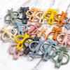 A collection of silicone teething toys in various pastel and earthy colors, including yellow, orange, pink, green, and gray.