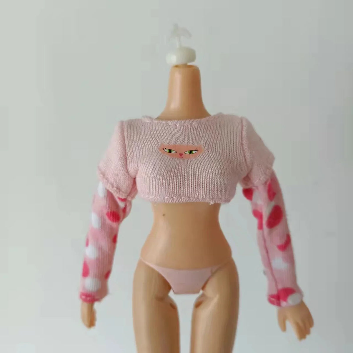 A pink knitted doll fashion set featuring a cropped top and long sleeves with pink and white floral patterns.