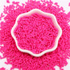 Pink polymer clay slice sprinkles in a white dish scattered on a pink background