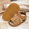 A pair of tan soft non-slip baby sandals for first walkers with textured soles resting on a wooden surface.