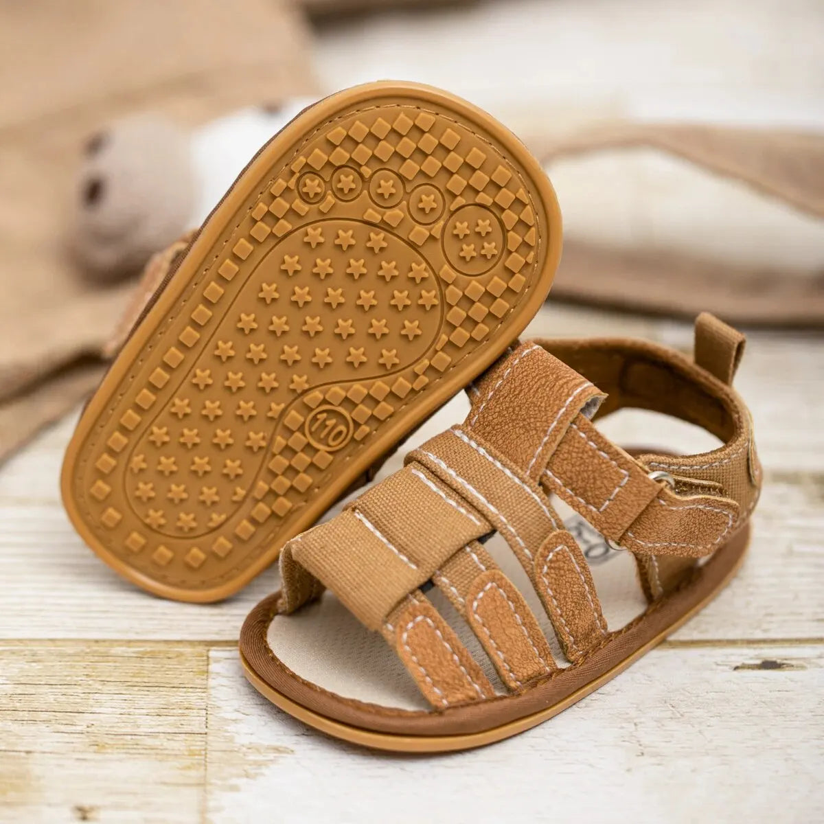 A pair of tan soft non-slip baby sandals for first walkers with textured soles resting on a wooden surface.