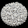 A close-up view of numerous white acrylic alphabet letter beads scattered on a dark background.