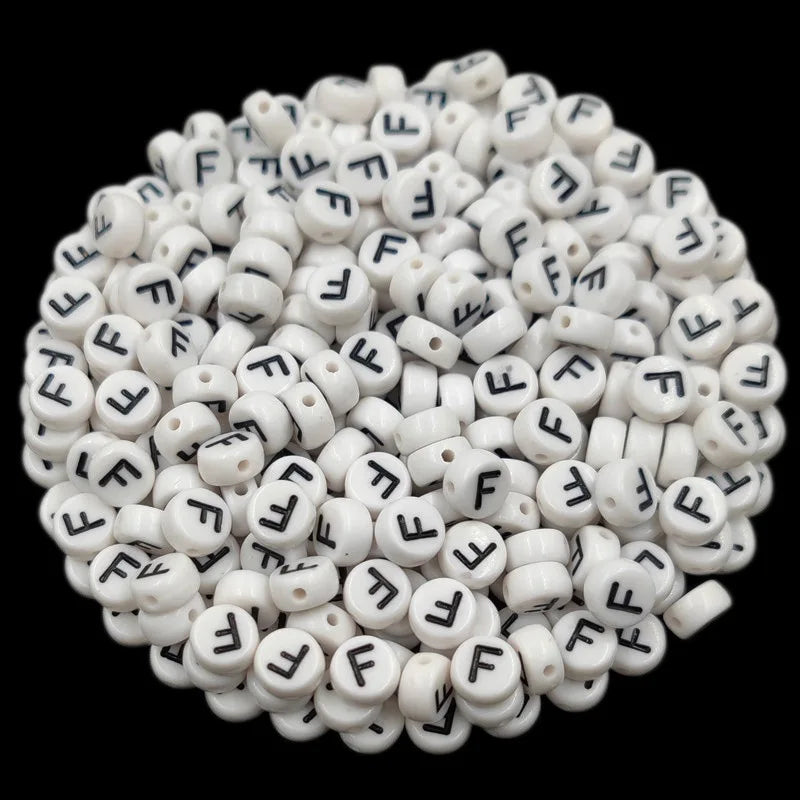 A close-up view of numerous white acrylic alphabet letter beads scattered on a dark background.