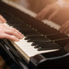 Hands playing a piano keyboard with note stickers on white and black keys.