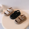 A pair of beige soft-soled sandals for toddlers, featuring light tan straps and black accents.