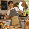 A smiling man wearing a grey chef apron is cooking in a kitchen, with a dog looking up.